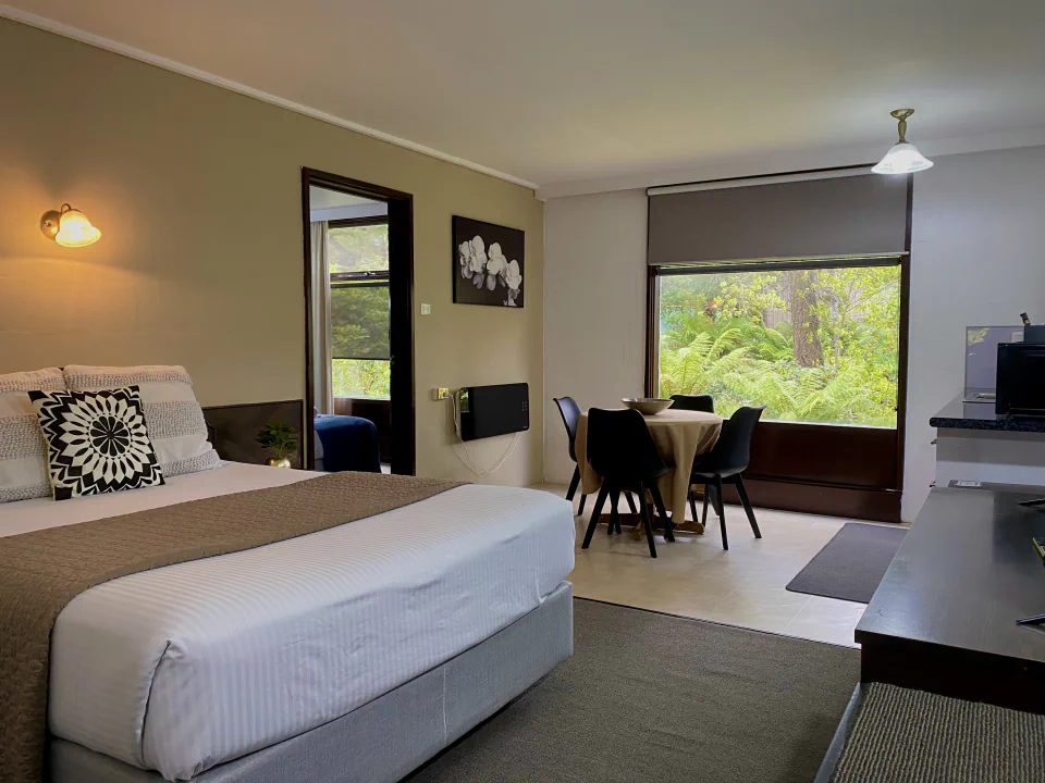 Queen bed and dining table beside a garden-facing window in the ground-floor suite